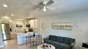 Uma sala de estar moderna com um sofá cinza, uma mesa de centro redonda e uma área de jantar com uma mesa e cadeiras de vidro.