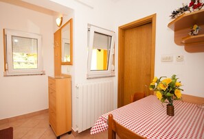 Ein kleiner Raum mit einem Holzschrank, einem Heizkörper, einem Tisch mit kariertem Tuch und einer Vase mit gelben Blumen.