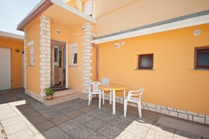 Ein Haus mit einer gefliesten Terrasse, einem Tisch mit Stühlen und einem kleinen Fenster.