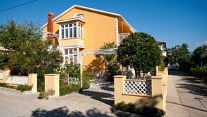 Ein zweistöckiges Haus mit gelber Fassade, einem Balkon und einem kleinen Garten.