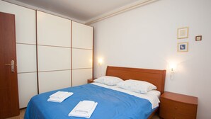 A neatly made bed with blue bedding and white pillows, a wooden nightstand with a lamp, and a wardrobe with a sliding door. - Only 300 metres to the great beach (Baska)