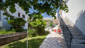 A stone pathway leading to a staircase with red chairs and a table, surrounded by greenery and a white building. - Only 300 metres to the great beach (Baska)