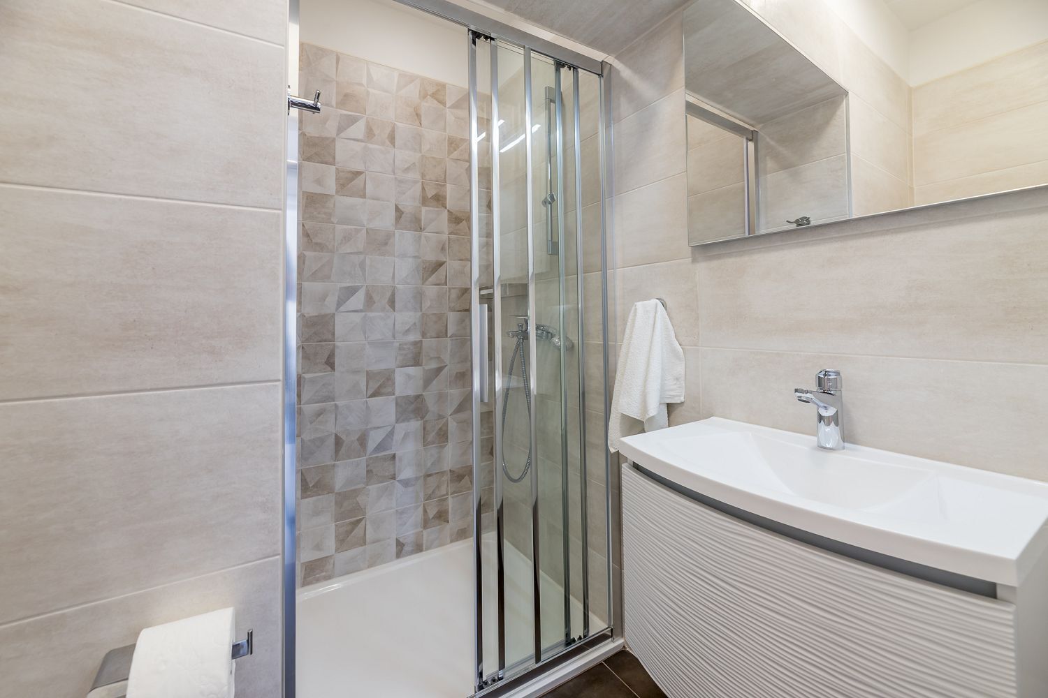 A modern bathroom with a glass shower enclosure, a white sink, and a tiled wall.