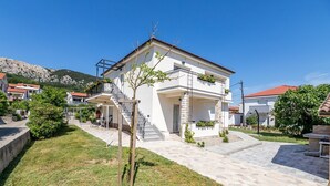 A two-story house with a stone facade, a balcony with plants, and a staircase leading to the entrance. - Only 300 metres to the fine pebble beach (Baska)