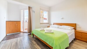 Ein Schlafzimmer mit einem Bett, einem Nachttisch aus Holz, einem Kleiderschrank und einer Schiebetür zum Balkon.