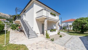 Ein modernes, zweistöckiges Gebäude mit Naturstein-Fassade, einer überdachten Außenbereiches mit Treppe und einem Garten mit kleinen Pflanzen und Blumen.