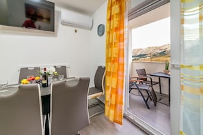 Een eethoek met een tafel gedekt voor twee personen, een televisie aan de muur en uitzicht op de omgeving via een schuifdeur.