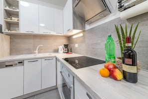 Una cocina moderna con armarios blancos, horno empotrado, cafetera y frutas frescas en la encimera.