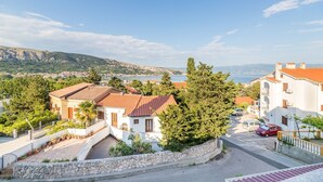 Zona residencial costera con casas, un muro de piedra y vistas al mar y colinas.