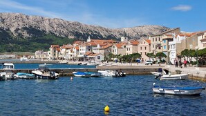 Un pueblo costero con edificios históricos, un puerto deportivo con barcos y montañas al fondo.
