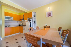 Cozinha compacta com armários laranjas, micro-ondas e geladeira. Há uma mesa de jantar com cadeiras e um vaso com flores.