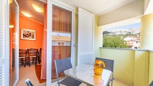 Un balcon avec une table, des chaises, une porte vitrée et une vue sur des bâtiments et de la verdure.