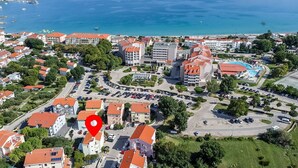 Une vue aérienne d’une ville côtière, avec un hôtel imposant doté d’un toit rouge, un parking et une vue sur la mer.