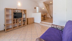 A living room with a television, wooden shelves, a purple sofa, and a staircase leading to another room. - Large terrace with sea view, beach 200 metres (Baska)