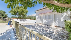 A white building with a tiled roof, a stone-paved courtyard, and a metal fence.