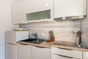 Cozinha moderna com armários brancos, pia de aço inoxidável e backsplash de mármore.