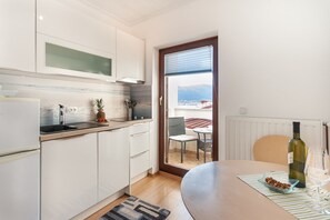 Cozinha moderna com armários brancos, bancada de madeira e vista para uma varanda com mesa e cadeiras.