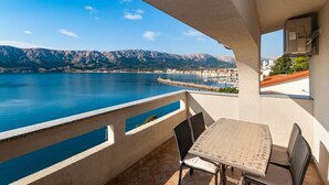 A balcony with a table and chairs overlooking a lake with mountains in the background. - Directly on the crystal clear Adriatic Sea (Baska)