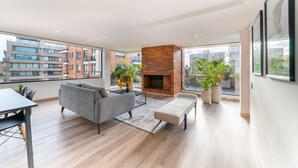 A modern living room with a brick fireplace, large windows, and a view of the cityscape. - Chicala By Wynwood House (Bogotá)