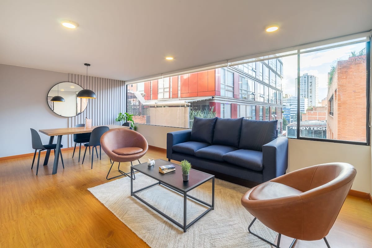 A modern living room with a sofa, two chairs, a coffee table, and a dining area with a table and chairs.