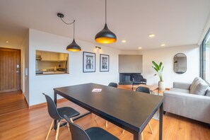 Een moderne woonkamer met een eettafel, zwarte stoelen, een grijze bank en een potplant.