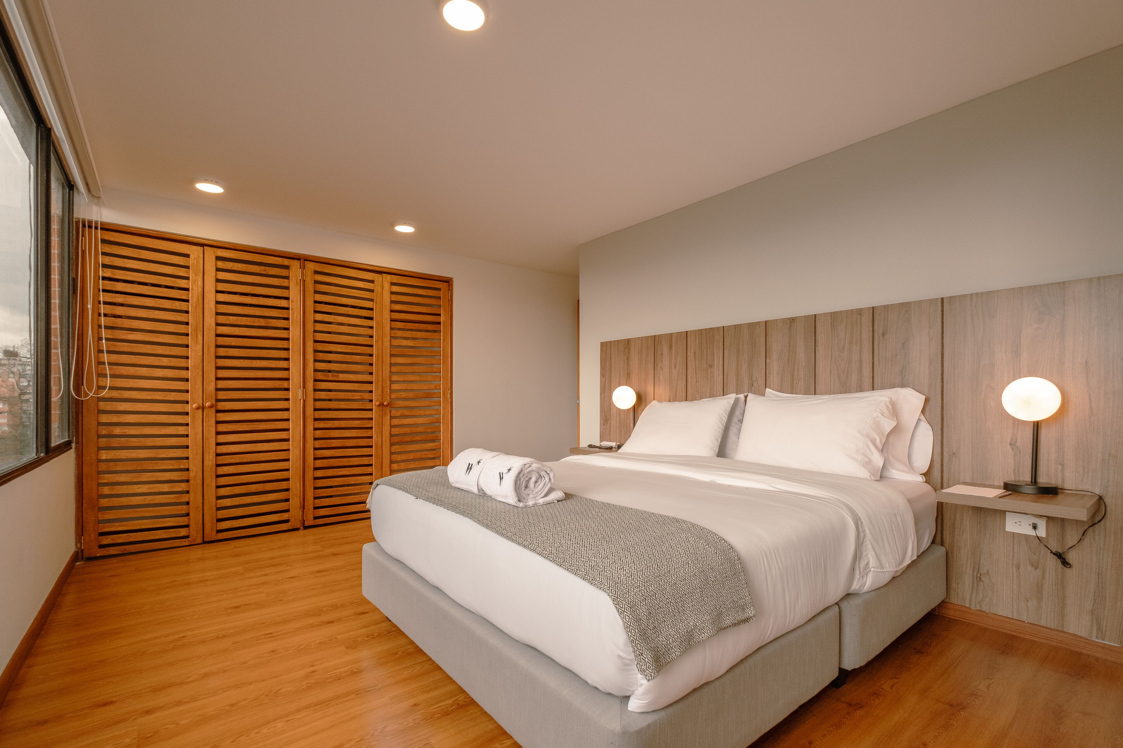 A modern bedroom with a large bed, wooden closet, and bedside lamps.