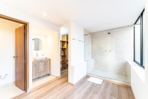 Een moderne badkamer met een houten wastafelmeubel, een glazen douchecabine en een inloopkast.