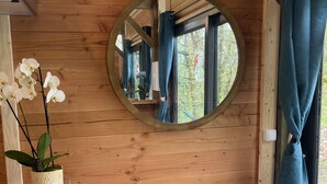 A wooden interior with a round mirror on the wall, a potted orchid, and a window with blue curtains.