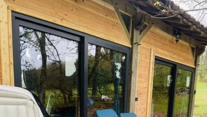 An outdoor hot tub with a wooden deck, a glass door, and a blue chair.
