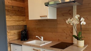 A compact kitchen with white cabinets, a stainless steel range hood, a built-in sink, and a coffee maker.