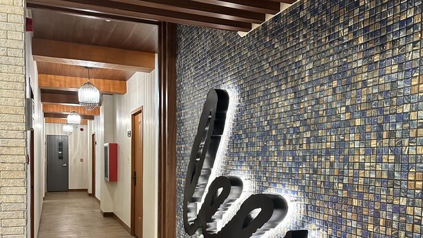 Un pasillo con un muro de mosaico, piso de madera y un letrero que dice 'Hotel'.
