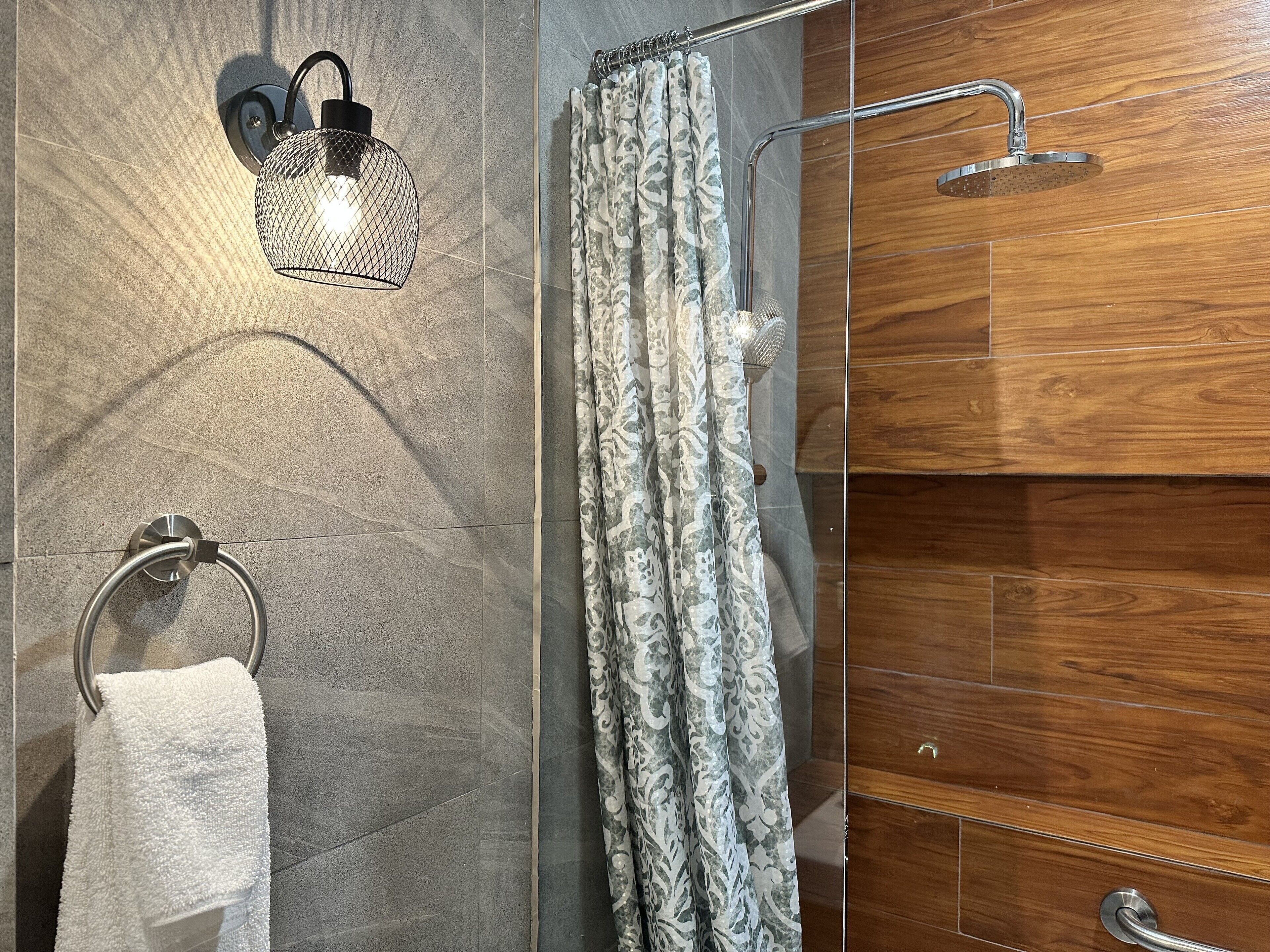 A modern bathroom with a shower, a towel rack, and a wall-mounted light fixture.
