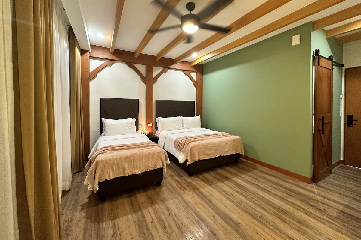 A room with two beds, wooden beams on the ceiling, a ceiling fan, and a green wall.