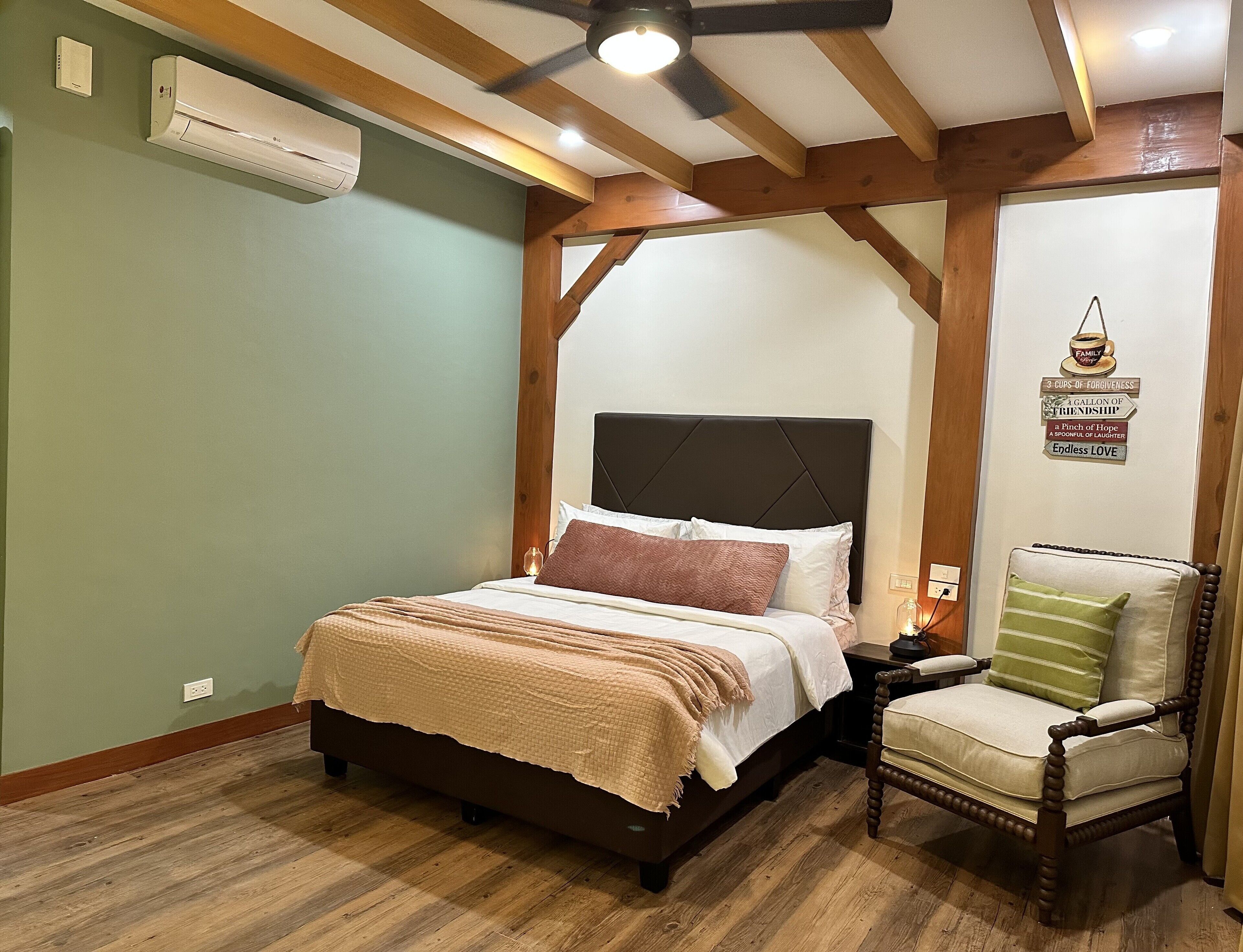 A bedroom with a bed, a nightstand, a chair, wooden beams, a ceiling fan, and an air conditioning unit.