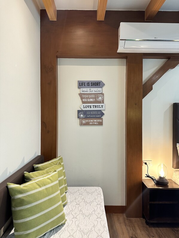 Une chambre à coucher avec un lit, des oreillers, un panneau mural affichant des conseils de vie, un climatiseur et une lampe de chevet.