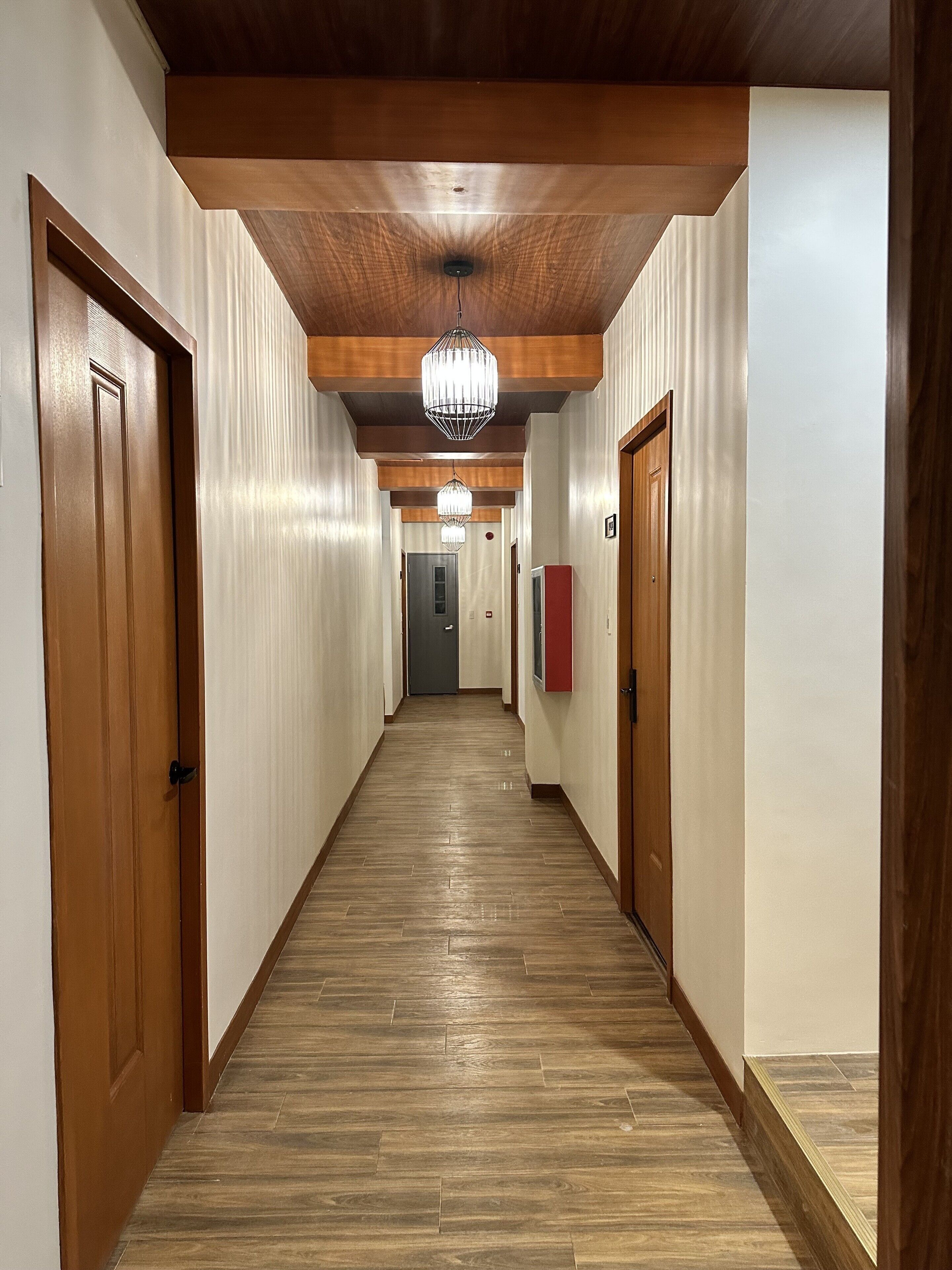 Un long couloir étroit, doté de planchers et de murs en bois, agrémenté d’un lustre et de portes en bois.