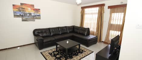 A living room with a black leather sectional sofa, a black coffee table, and a flat-screen TV on a stand.
