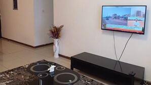 Una sala de estar con una televisión de pantalla plana montada en la pared, un mueble de entretenimiento negro, una mesa de centro y un jarrón decorativo.