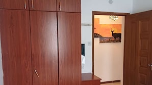 Una habitación con un armario de madera grande, un escritorio pequeño y una puerta que da a otra habitación con un cuadro de atardecer.