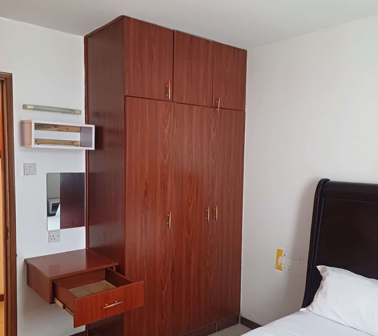 Une chambre à coucher avec une armoire en bois, une table de chevet, un lit et un miroir.
