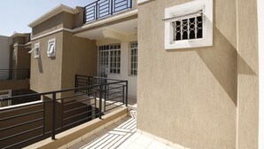 Un edificio residencial con balcón, una ventana con celosía decorativa y una escalera que sube a un nivel superior.