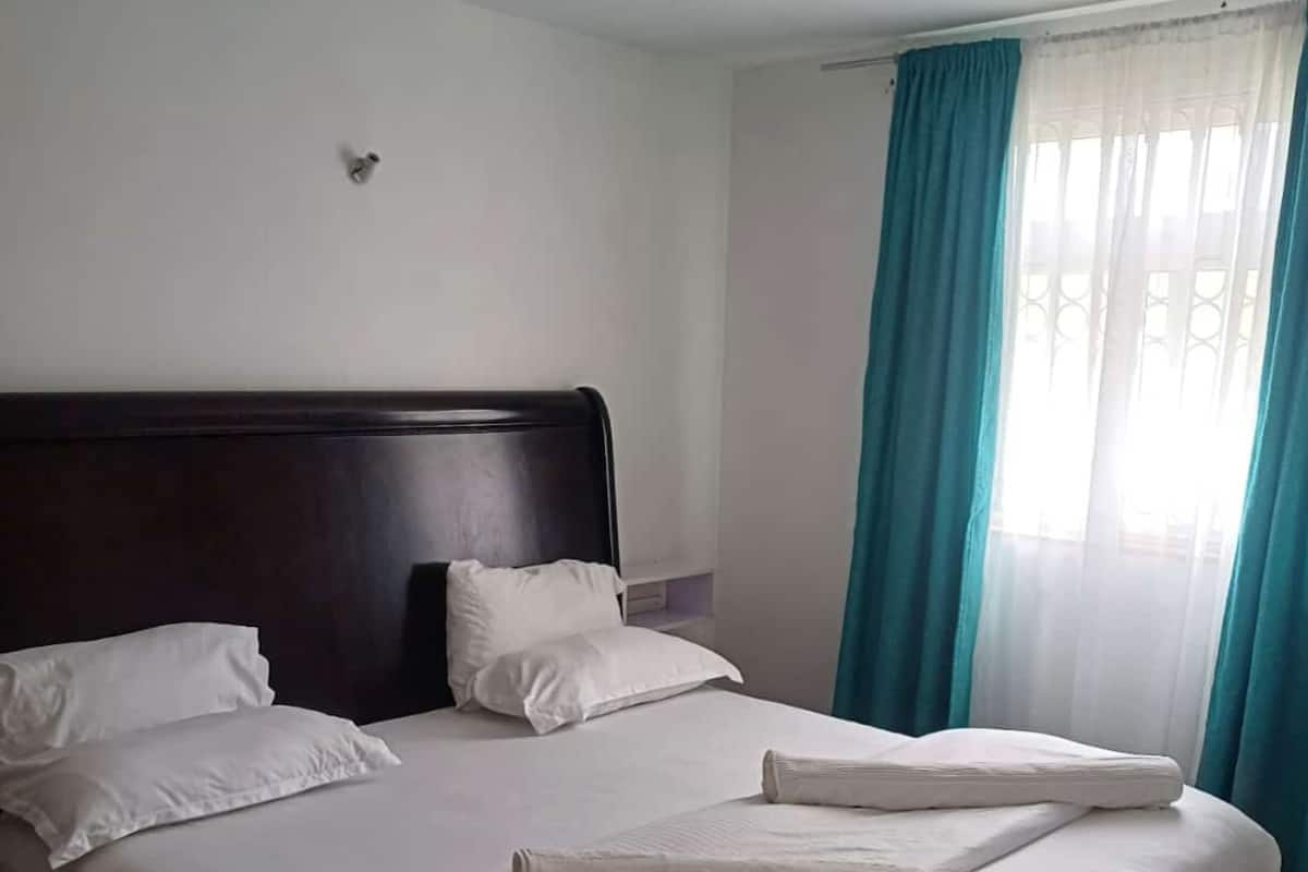 A neatly made bed with white linens and pillows, a dark wooden headboard, and a window with blue curtains.