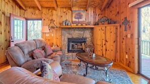 L’intérieur d’un chalet en bois chaleureux, avec une cheminée en pierre, un canapé en cuir et une grande fenêtre.