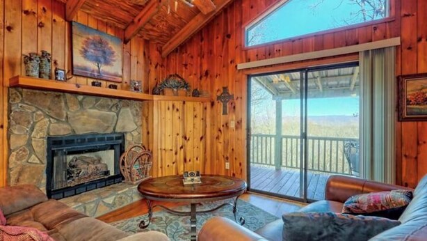 L’intérieur chaleureux d’un chalet avec une cheminée en pierre, des canapés en cuir et une grande fenêtre donnant sur une terrasse.