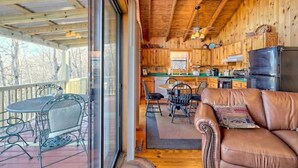 L’intérieur chaleureux d’un chalet, avec un revêtement mural en bois, un coin repas doté de chaises en métal, un canapé en cuir et une cuisine avec des meubles en bois et un réfrigérateur.