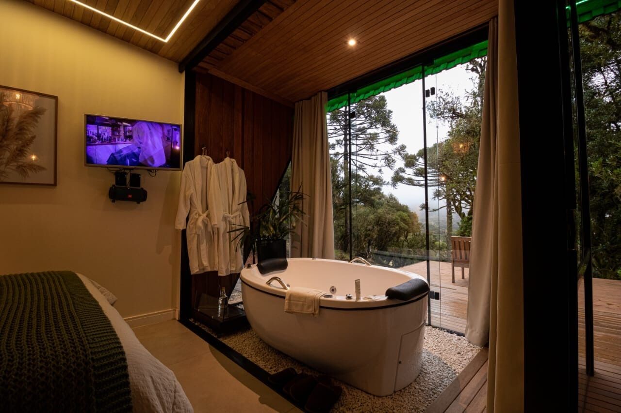 A modern bathroom with a freestanding bathtub, a television, and a large window with a view of trees.