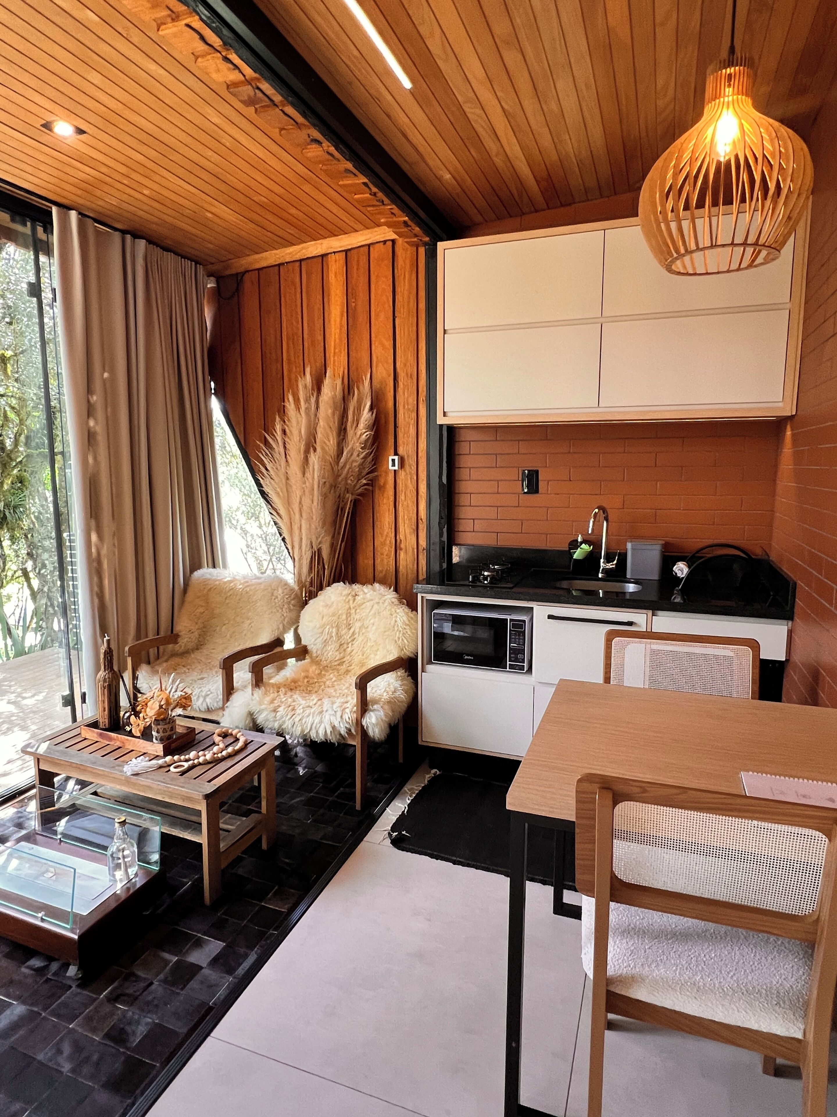 Uma cozinha moderna com micro-ondas, fogão e armários, uma área de refeições com mesa e cadeiras, e um espaço de estar acolhedor com uma poltrona e um vaso decorativo.