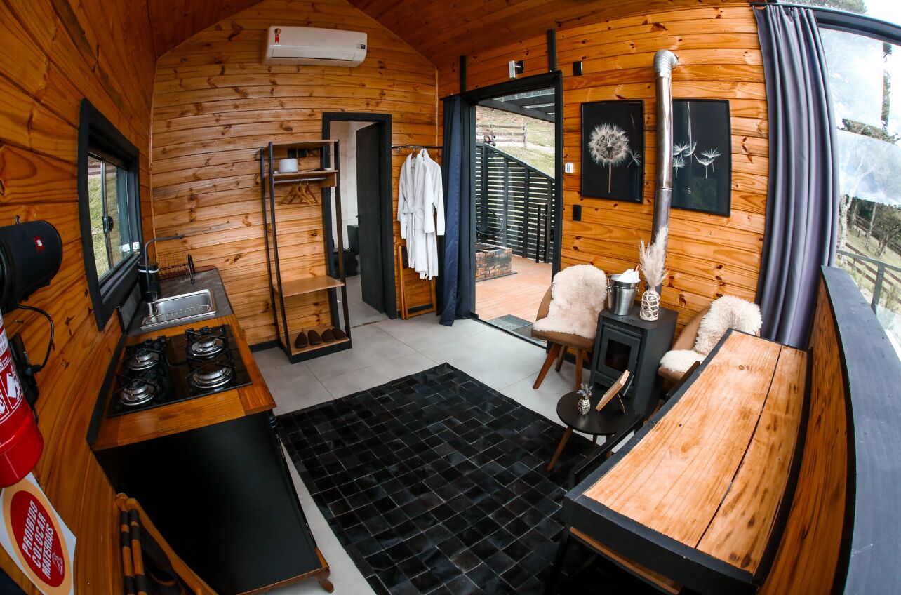 A cozy cabin interior with a wooden interior, a stove, a dining table, and a view through the door.