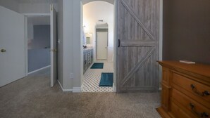 Una habitación con puerta cerrada, un aparador de madera y un pasillo que da a una zona de cocina.