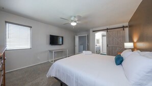 Una habitación de hotel con una cama grande, un ventilador de techo, un televisor y una puerta corrediza de estilo rústico.